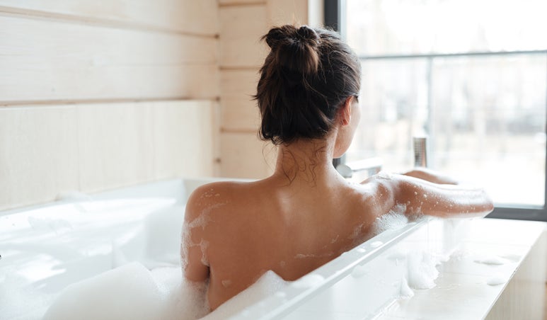 Mujer haciendo baño de asiento en casa con agua tibia y velas relajantes